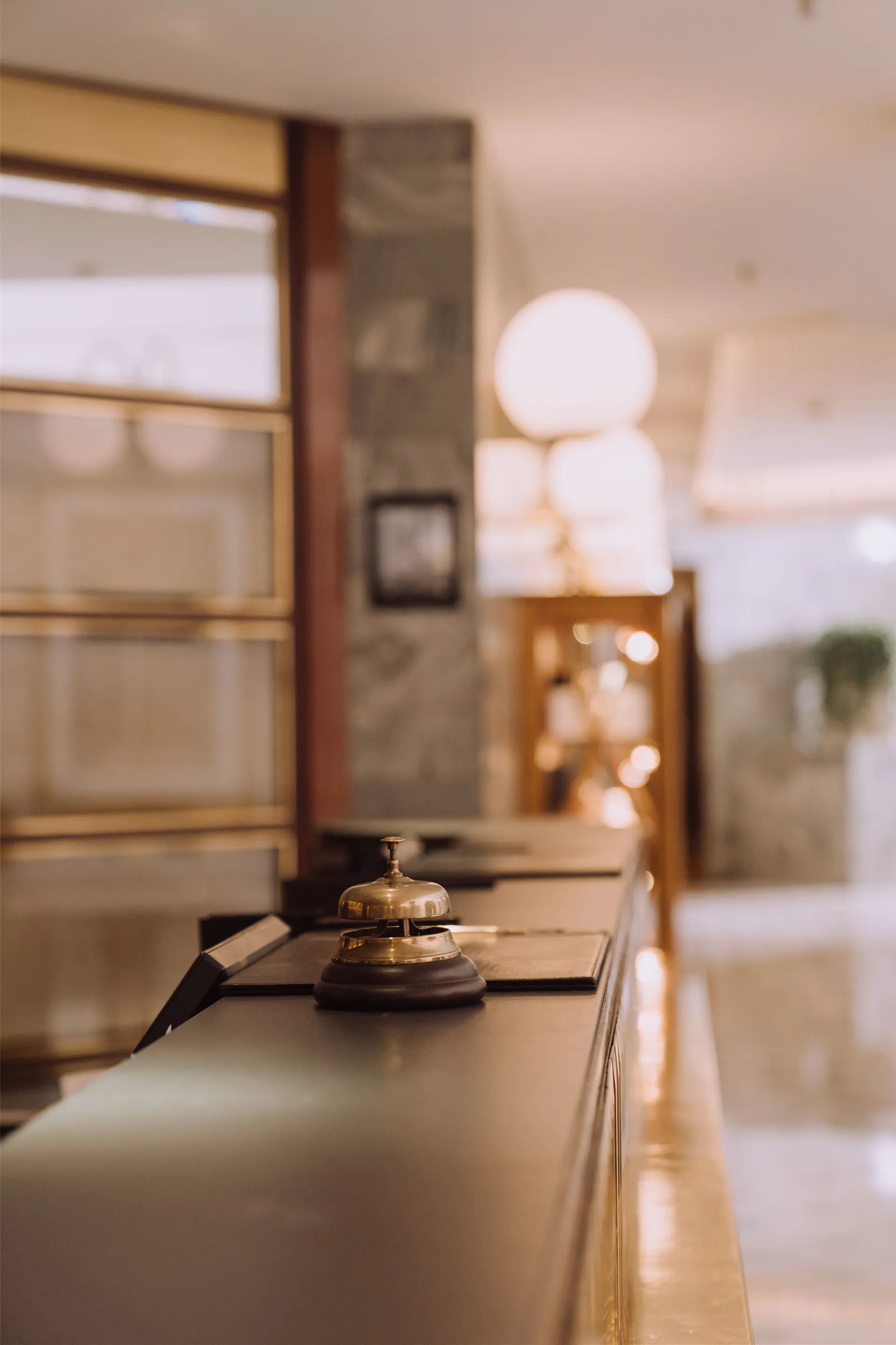 A close-up view of a hotel reception counter with a classic bell and warm lighting.